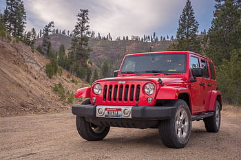 Red Jeep parked on dirt road with mountainous forest backdrop, ideal for travel and adventure themes. HD wallpaper