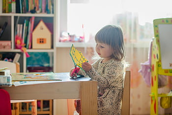 A young girl in a bright classroom engaged in a creative arts and crafts project at a table. HD wallpaper