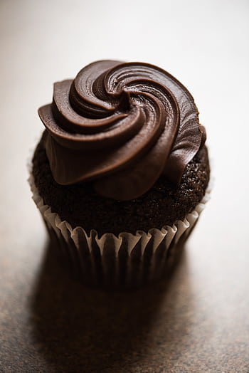 Delicious chocolate cupcake topped with rich, creamy frosting in a cozy indoor setting. HD phone wallpaper