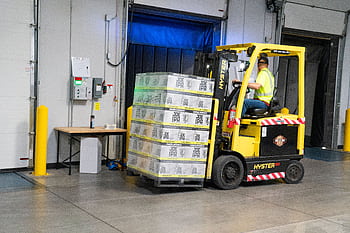 A warehouse employee operating a forklift to move stocked goods indoors. Perfect for industry and logistics visuals. HD wallpaper