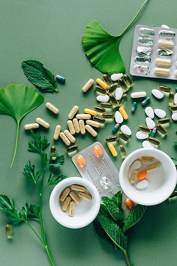 Flat lay of assorted pills and herbs on green surface, symbolizing health and wellness. HD phone wallpaper