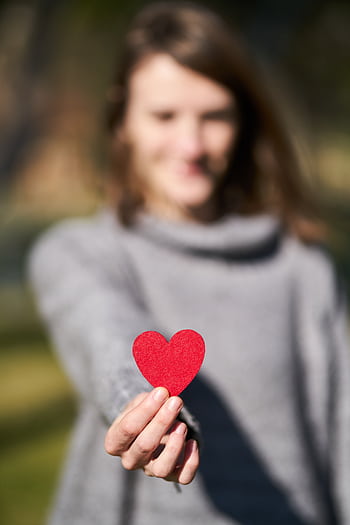 A woman presenting a red heart symbol, showcasing love and compassion. HD phone wallpaper