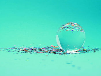A crystal sphere sits atop colorful glitter on a vibrant turquoise background, creating a lively and artistic composition. HD wallpaper