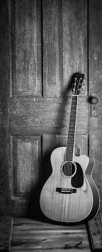 A classic acoustic guitar leaning against a rustic wooden door in a black and white vintage style. HD phone wallpaper