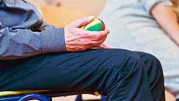Elderly man holding a colorful therapy ball indoors, promoting relaxation and health. HD wallpaper