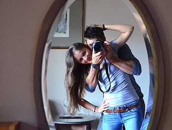 Smiling couple capturing a joyful moment with a mirror selfie indoors. HD wallpaper