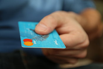 A close-up shot of a hand offering a blue debit card for payment. HD wallpaper