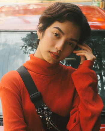 Portrait of a woman in a red turtleneck posing outdoors with a car in the background. HD phone wallpaper