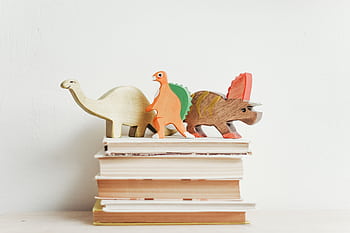 Colorful wooden dinosaurs on top of a stack of hardcover books on a light background. HD wallpaper