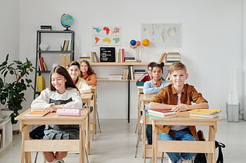 A group of happy students sitting at desks in a modern classroom environment. HD wallpaper