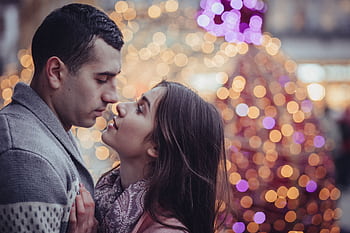 A loving couple embraces amidst festive holiday lights, capturing a moment of romance and holiday spirit. HD wallpaper