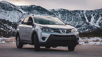 A silver SUV is parked in front of stunning snow-covered mountains during daytime. HD wallpaper