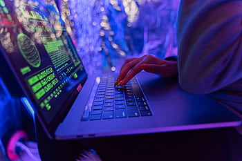 Close-up of hands typing on a laptop displaying cybersecurity graphics, illuminated by purple light. HD wallpaper