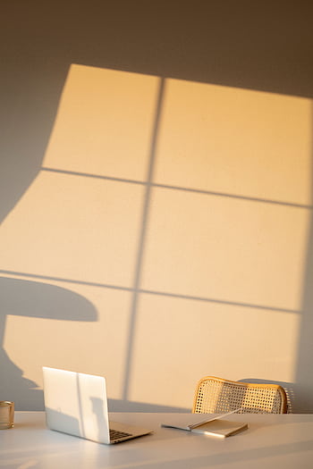 A serene minimalist workspace with natural light casting shadows on a wall, featuring a laptop. HD phone wallpaper