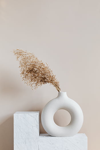 Elegant ceramic vase with dried grass on a marble pedestal, showcasing simplicity and minimalism. HD phone wallpaper