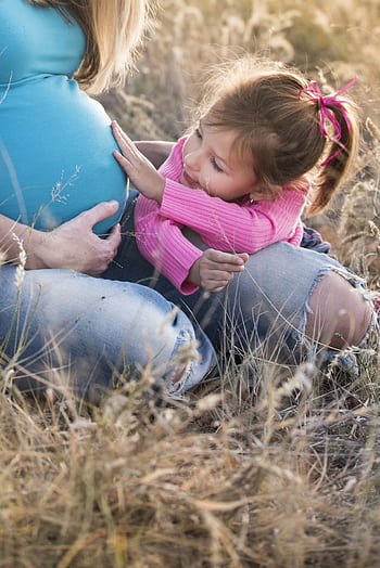 Pregnant woman with child sharing a tender moment in a grassy field. HD phone wallpaper