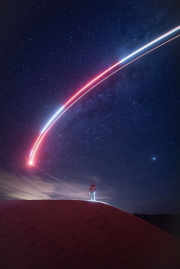 A person under a starry night sky with a striking light trail across the horizon. HD phone wallpaper