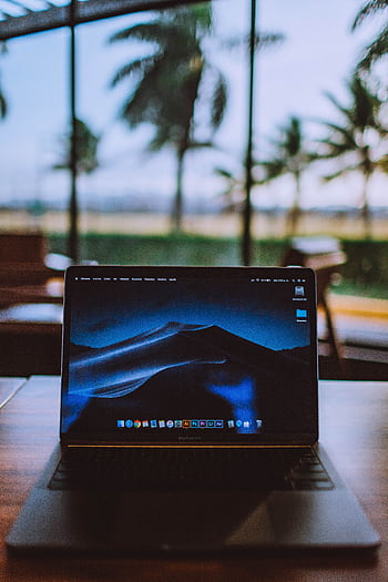 A sleek laptop on a wooden desk with a tropical view behind, ideal for remote work and travel themes. HD phone wallpaper
