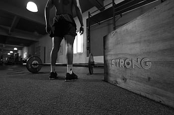 Black and white of a man in a gym with barbell and 'Strong' box. HD wallpaper