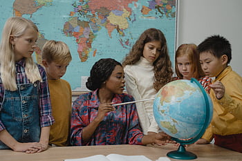 Diverse elementary students learning geography with a teacher and globe in the classroom. HD wallpaper