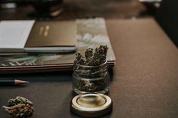A close-up of cannabis buds in a glass container on a desk, emphasizing a natural and relaxed setting. HD wallpaper