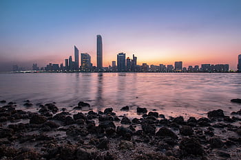 Stunning Abu Dhabi cityscape at sunrise with calm ocean foreground and vibrant sky. HD wallpaper