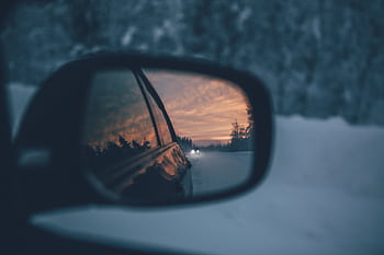 A scenic winter drive captured through a car's side mirror during sunset, reflecting snowy roads and trees. HD wallpaper