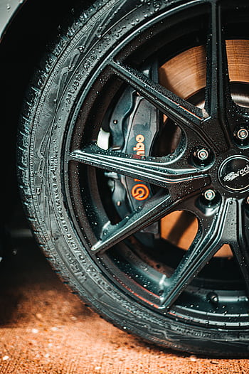 Detailed of a black alloy wheel with visible water droplets and a prominent Brembo brake caliper. HD phone wallpaper
