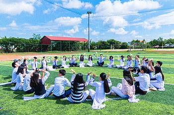 Students seated in a circle on a school field engaging in outdoor activities. HD wallpaper