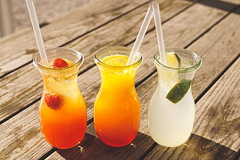 Close-up of three refreshing beverages with citrus, strawberries, and lime on a sunny wooden table. HD wallpaper