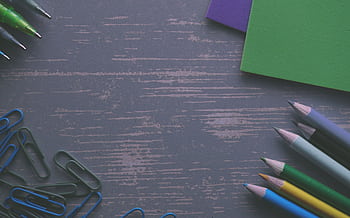 A flat lay of colored pencils, paper clips, and paper on a wooden desk. HD wallpaper