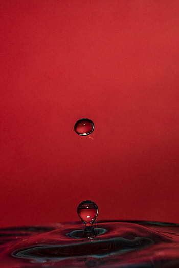 A captivating close-up of a water drop creating ripples on a red backdrop. Perfect for backgrounds. HD phone wallpaper