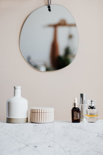 A set of luxury skincare products on a marble shelf with a blurred round mirror reflecting in the background. HD phone wallpaper