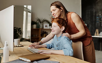 A mother and her child smiling while using a computer at home, focused on learning. HD wallpaper