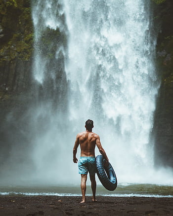 A man enjoying the natural beauty of a waterfall in Bali, Indonesia, holding a lifebuoy. HD phone wallpaper