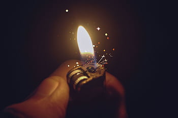 Intense close-up of a lighter igniting a bright flame with spark effects against a dark background. HD wallpaper