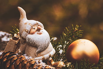 A charming Christmas gnome decoration with a golden ornament among pine needles. HD wallpaper
