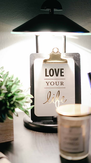 A warmly lit desk setup featuring a lamp, inspirational clipboard, and decor for a cozy ambiance. HD phone wallpaper