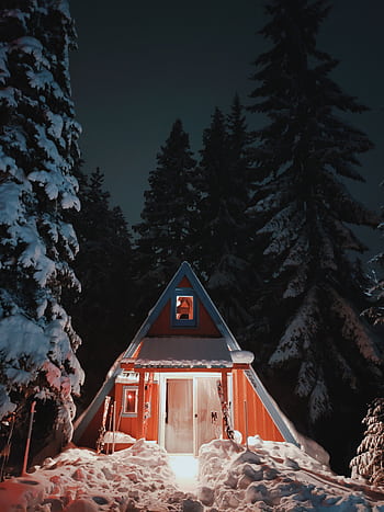 A beautifully lit A-frame cabin amidst a snowy forest, creating a serene winter night scene. HD phone wallpaper