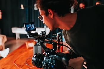Man filming on set with professional video camera in studio setting. HD wallpaper