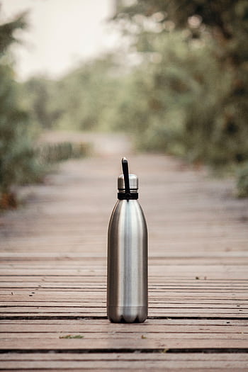 A stainless steel water bottle on a wooden path in an outdoor setting, surrounded by greenery. HD phone wallpaper