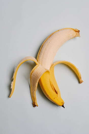 Ripe banana peeled halfway on a light pastel background, perfect for healthy eating themes. HD phone wallpaper