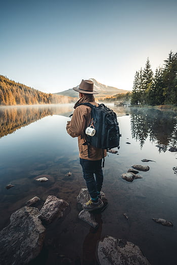 A hiker with a backpack stands by a tranquil mountain lake, capturing the essence of adventure and serenity. HD phone wallpaper