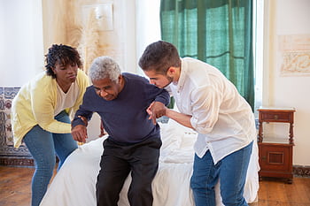 An elderly man receiving assistance from caregivers in a cozy home environment. HD wallpaper
