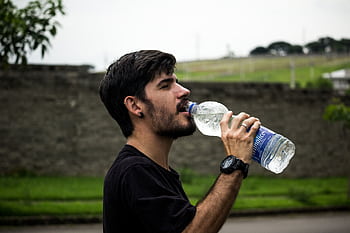 A young man drinks bottled water outside, staying hydrated and refreshed. HD wallpaper