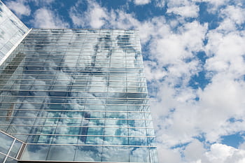 A contemporary skyscraper with glass panels reflecting a bright cloudy sky. HD wallpaper