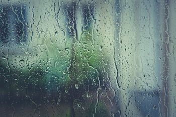 Close-up of raindrops on a window with a blurred natural backdrop, evoking a rainy day mood. HD wallpaper
