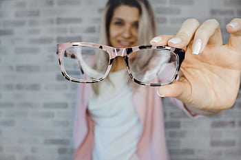 Young woman with blonde hair holding eyeglasses indoors, focusing on vision aid. HD wallpaper