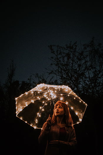 A woman holding a lit umbrella in a dark outdoor setting creating a moody night portrait. HD phone wallpaper