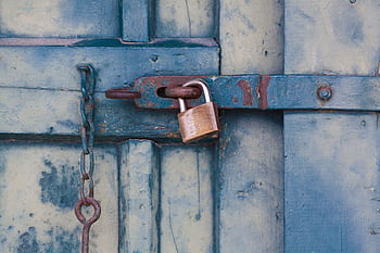 A close-up of a rusty padlock securing a blue painted wooden door with chain and bolt. HD wallpaper
